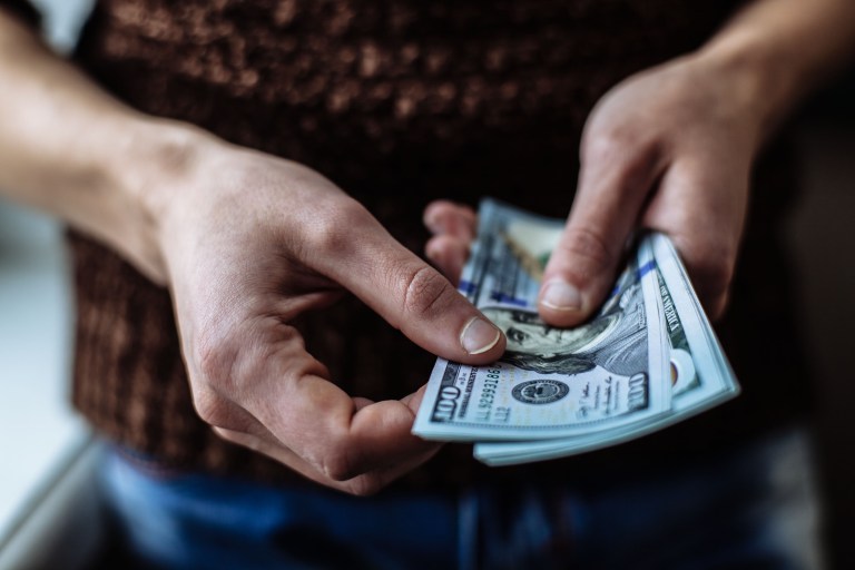 man holding multiple one hundred dollar bills in hands