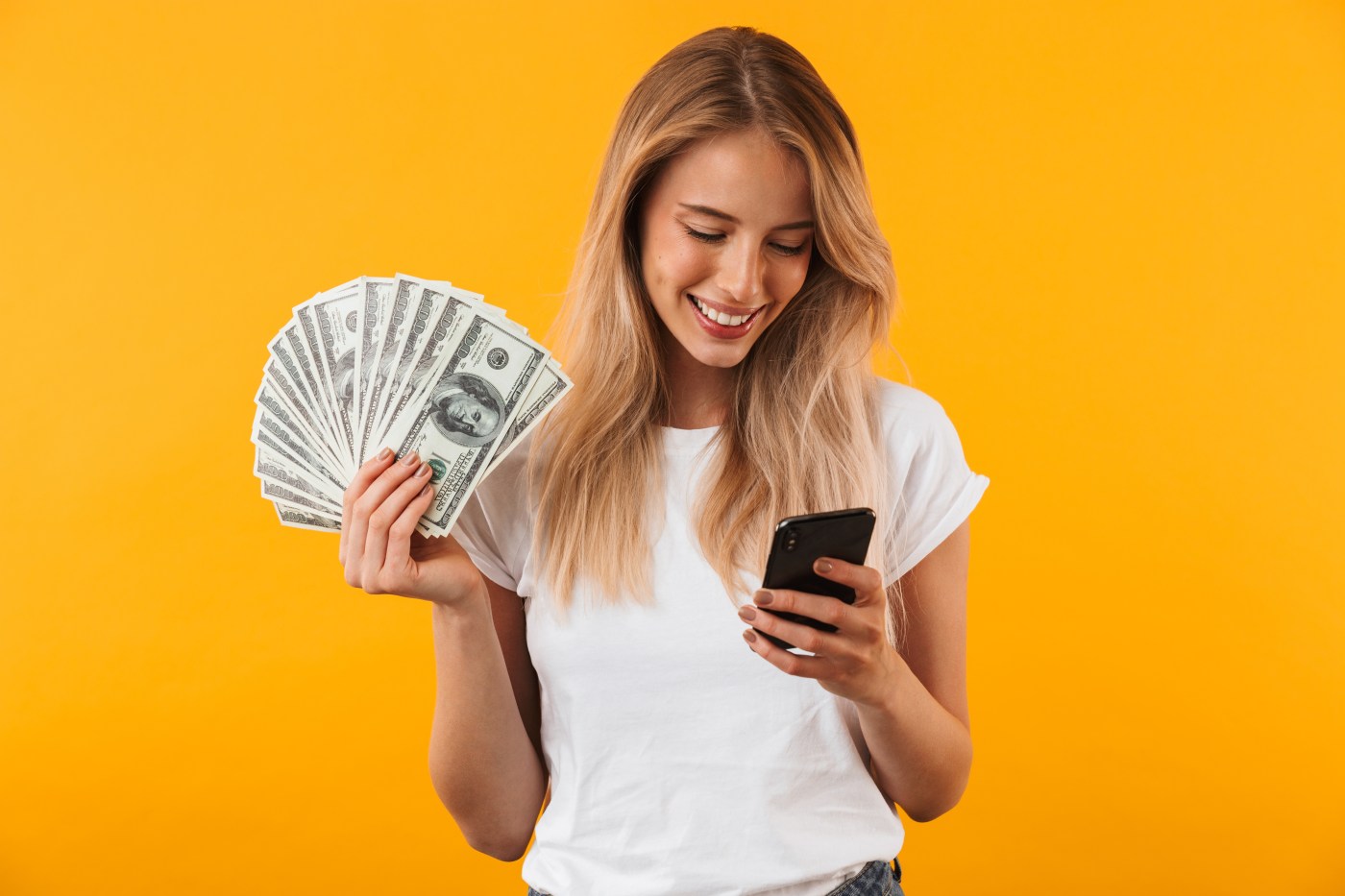 Young woman holding money and looking at her phone