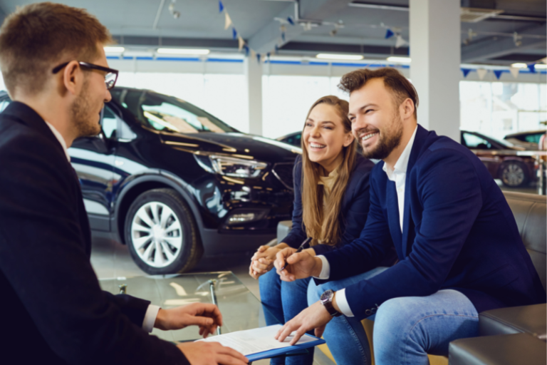 Young couple smiling at car salesman inside of car dealership