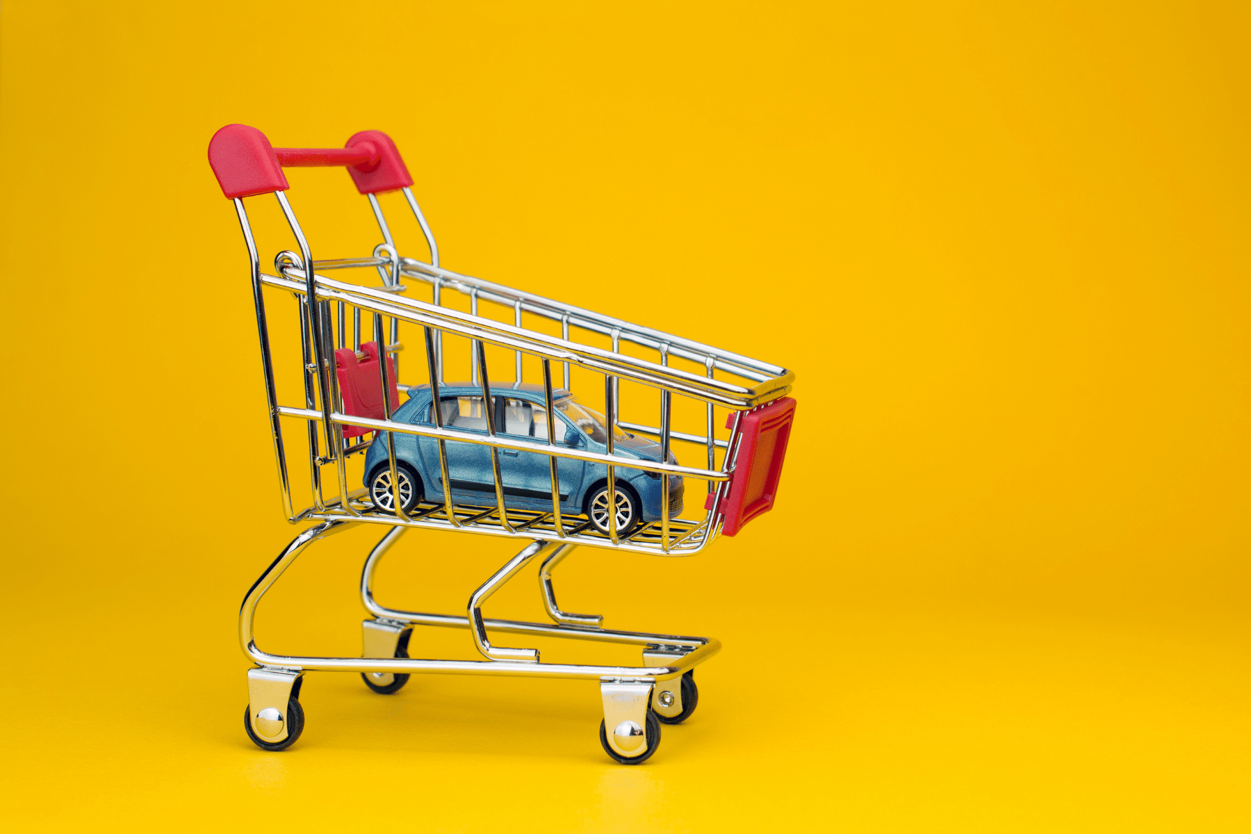 Blue toy car inside shopping cart in front of yellow backdrop