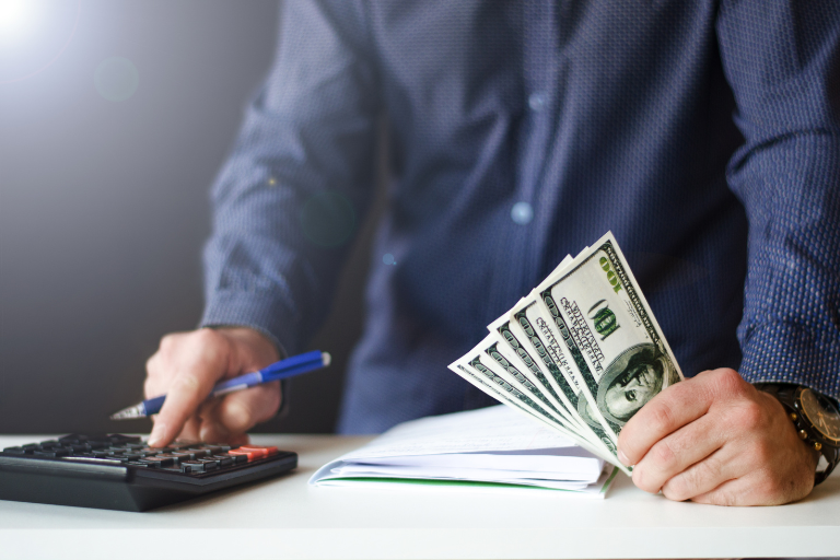 Man holding money and a pen while typing on calculator