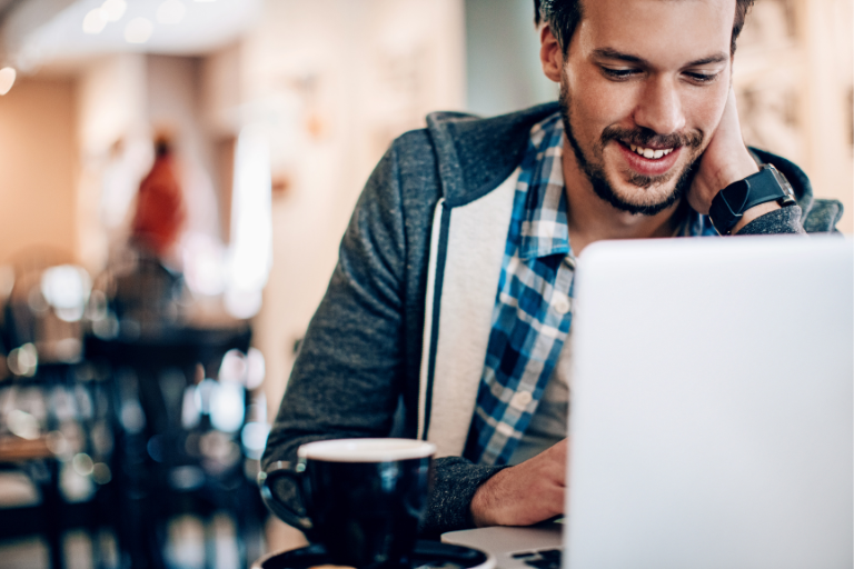 Smiling man sitting at table in coffee shop working on computer