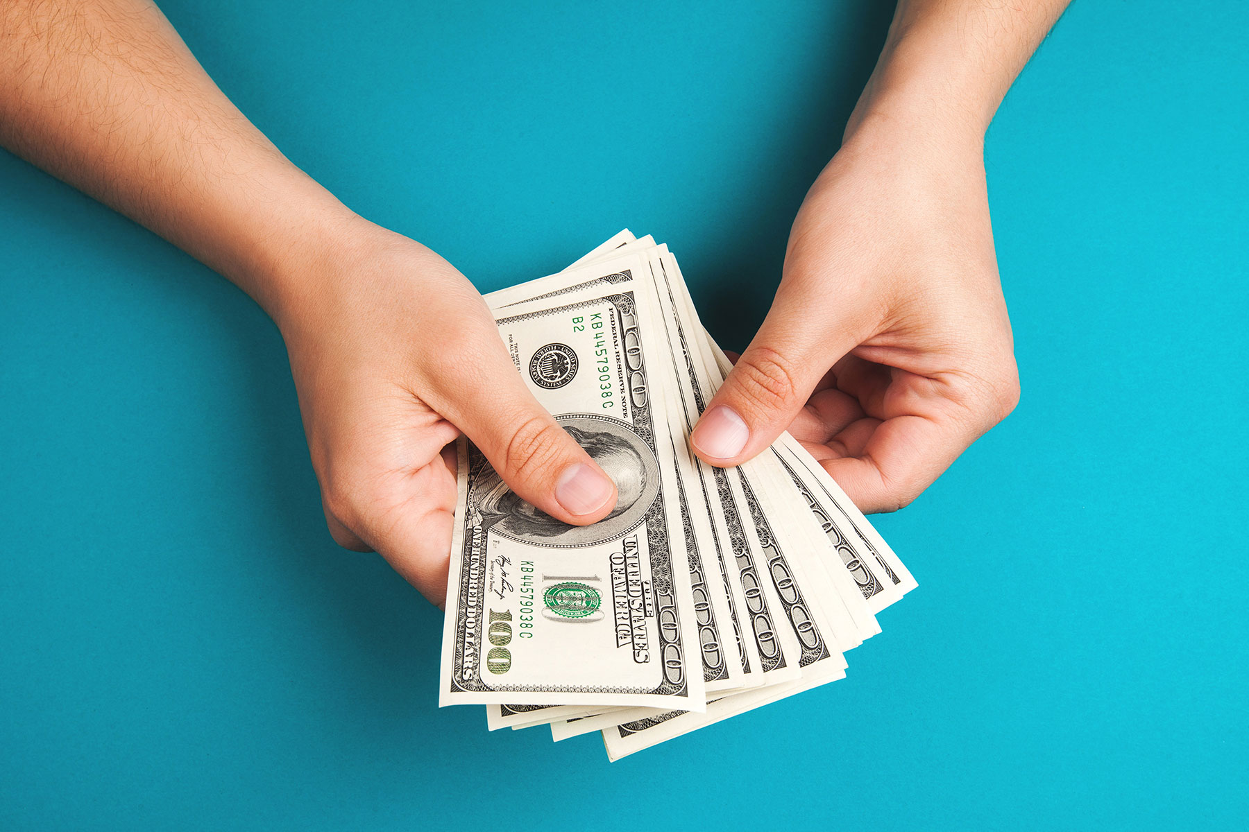 Hands holding money over a bright blue background