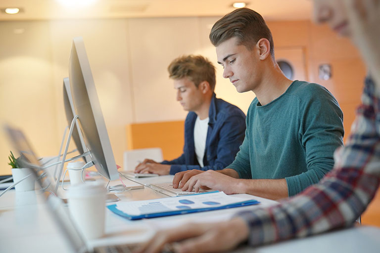 Group of male students in class working on computers, looking serious