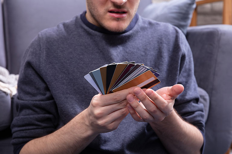 Man looking confused, staring at a large amount of credit cards he has fanned out in one hand