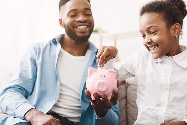 Dad and daughter putting coins into a pink piggy bank