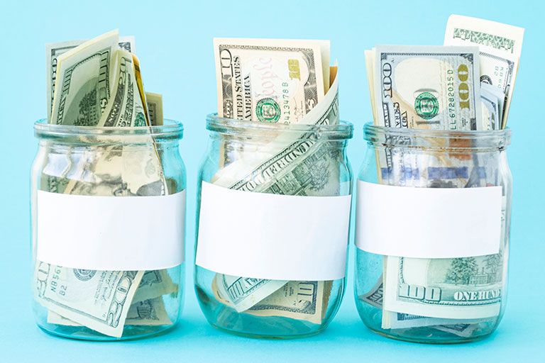 American dollars filling three clear jars with white labels on light blue background