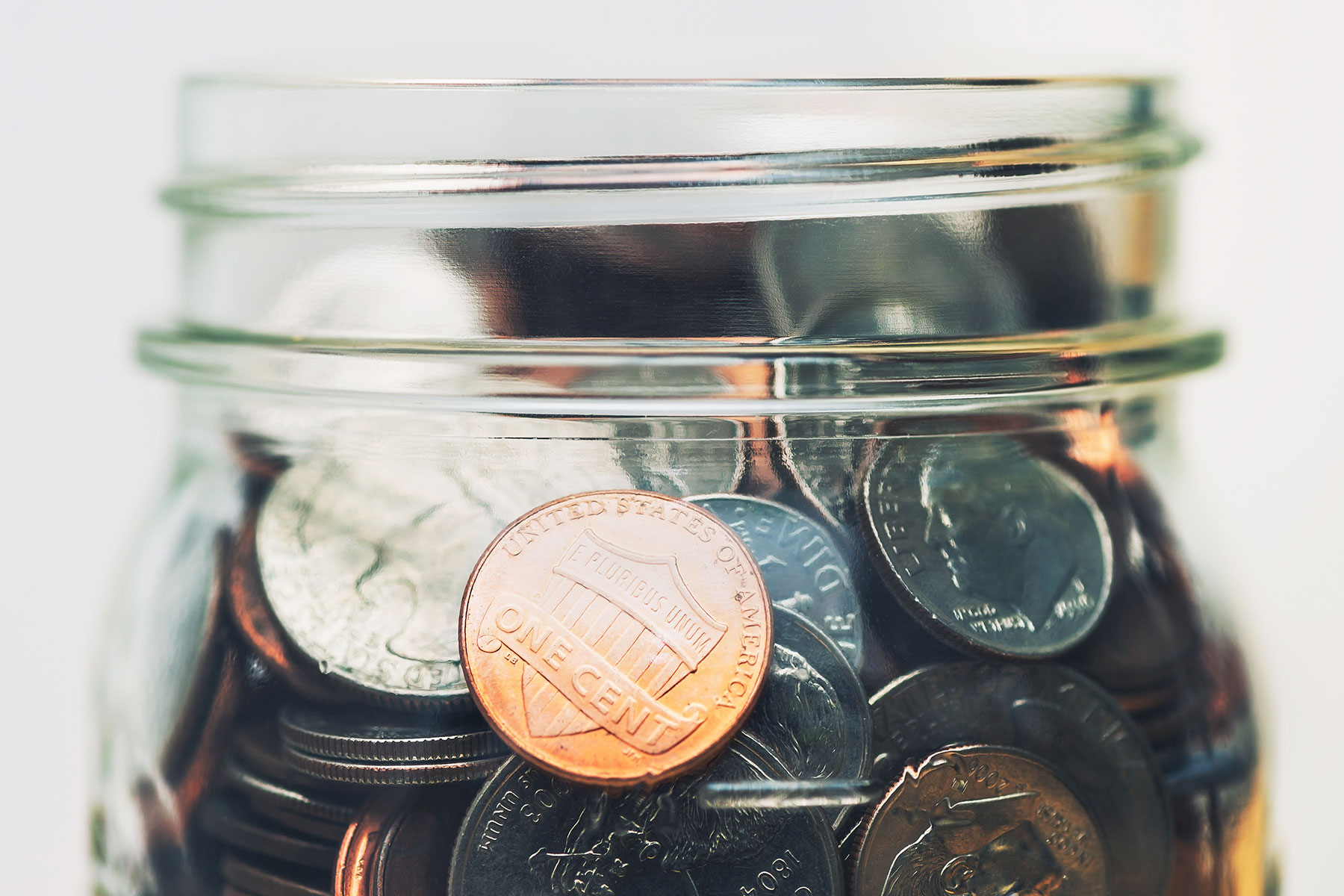 American coins in a clear glass mason jar up close in front of gray background