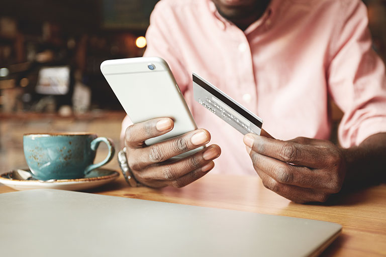 African American man in pink dress shirt paying with credit card online using his mobile phone
