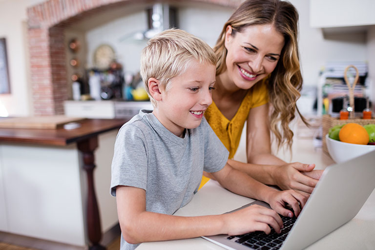 Mom teaching young son how to do something on a laptop computer