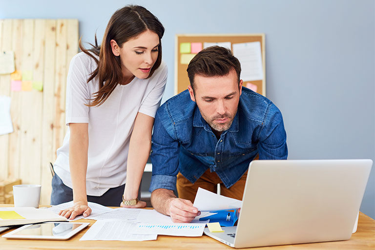 Woman looking over man's shoulder at a computer as with work on paying household bills