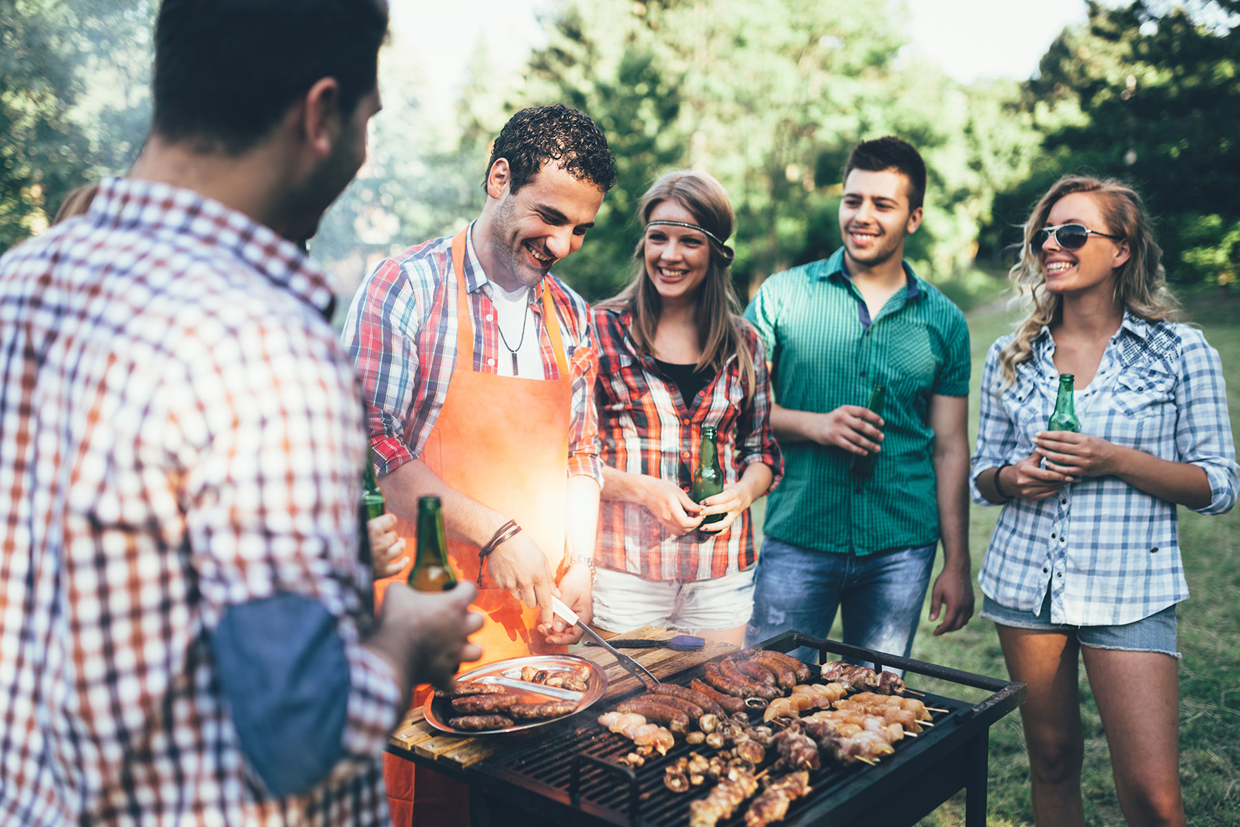 Group of friends wearing plaid shirts gathered around an outdoor grill filled with meat
