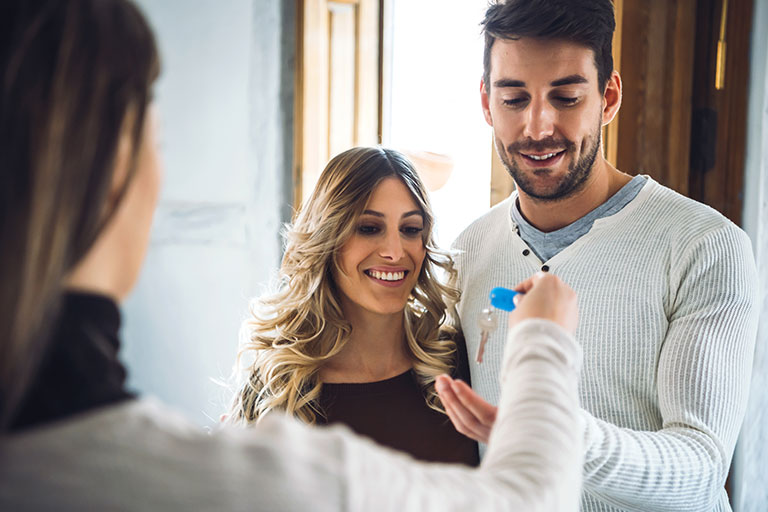 Woman handing house key to young couple