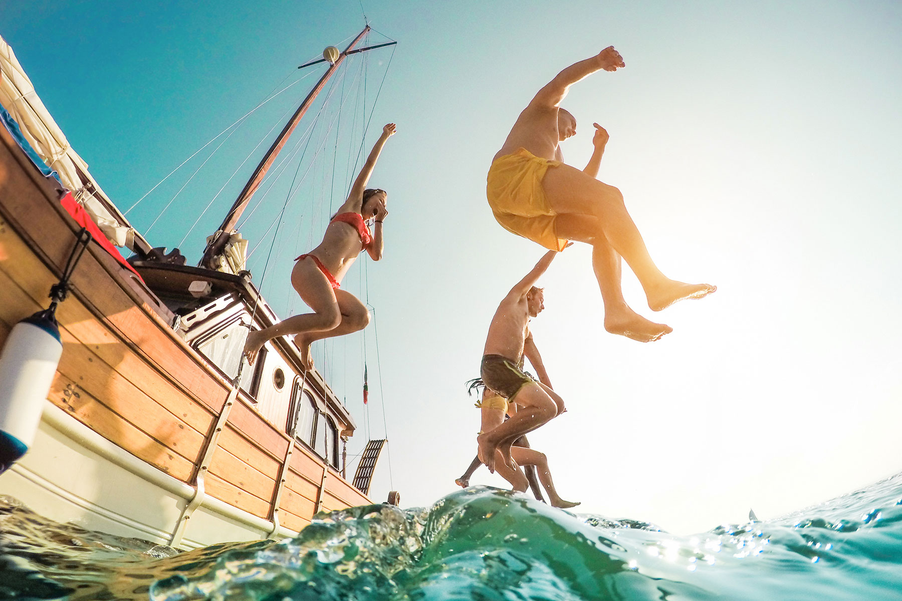 Group of friends jumping off a nice wooden boat into the open sea